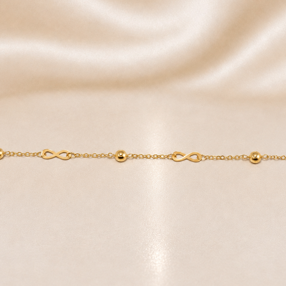 Gold bracelet with infinity symbols on a beige satin background 19.2K Portuguese Gold | Dainty Infinity & Ball Bracelet