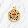 Gold pendant with 'Deus Te Abenção' text and red cross on a white fabric background 19.2K Portuguese Gold | Deus te Abencoe Charm