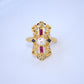 Gold ring with a pearl and red gemstones on a light blue background