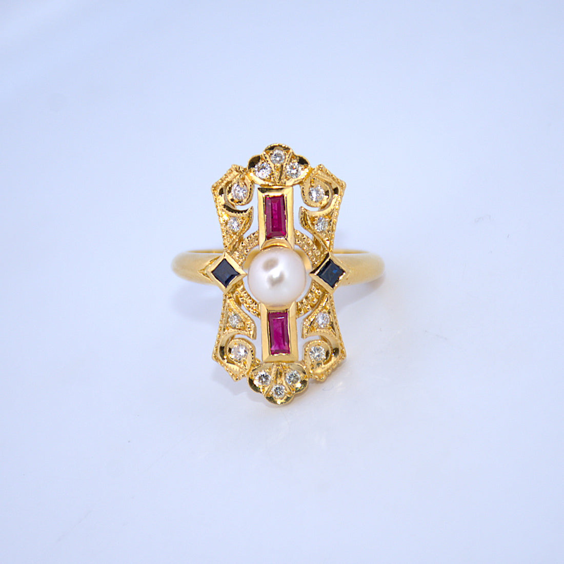 Gold ring with a pearl and red gemstones on a light blue background