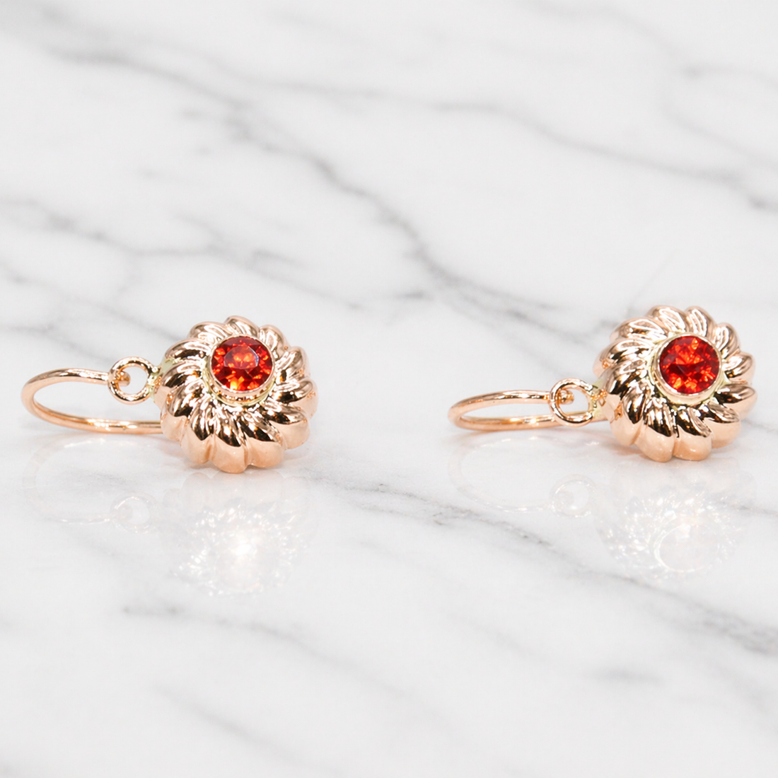 19.2k Portuguese Rose gold earrings with red gemstones on a marble surface