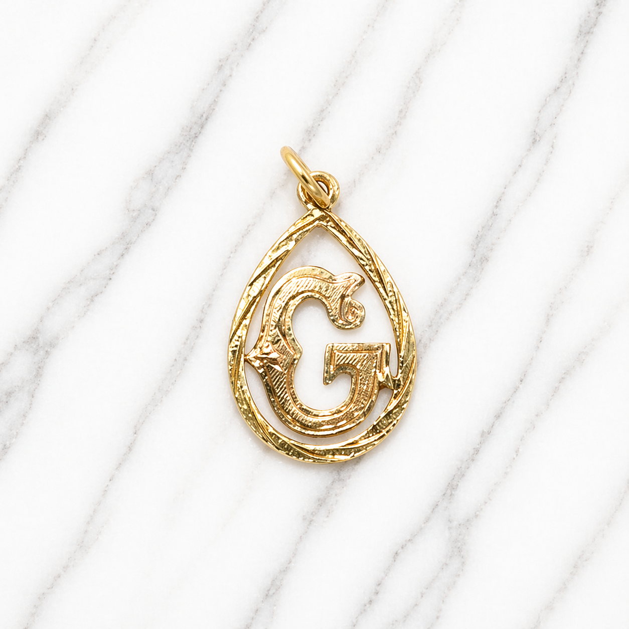Gold pendant with a letter 'G' design on a marble surface 19.2K Portuguese Gold | Tear Drop Letters 
