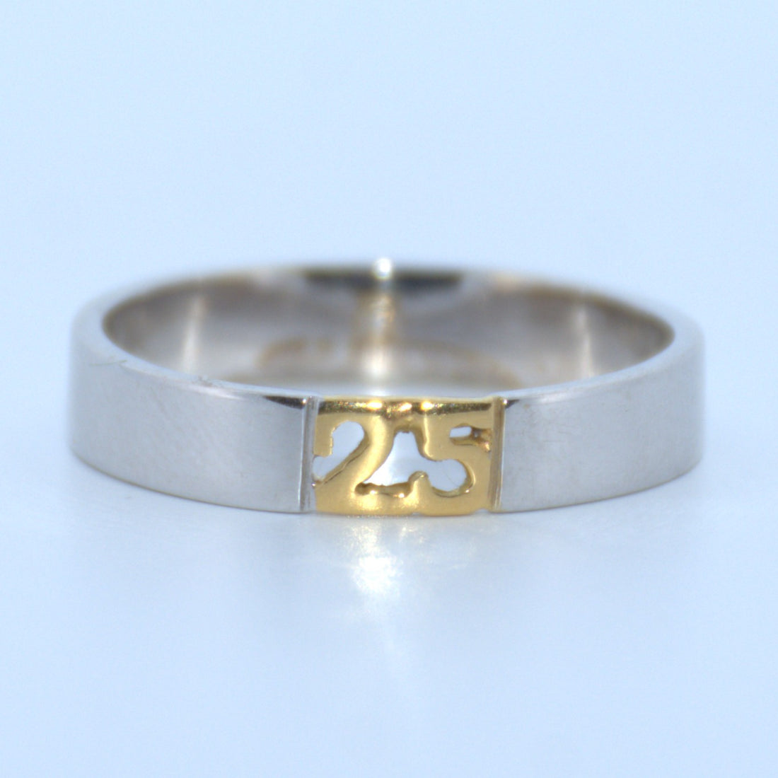 Silver ring with a gold '25' cutout on a light blue background
