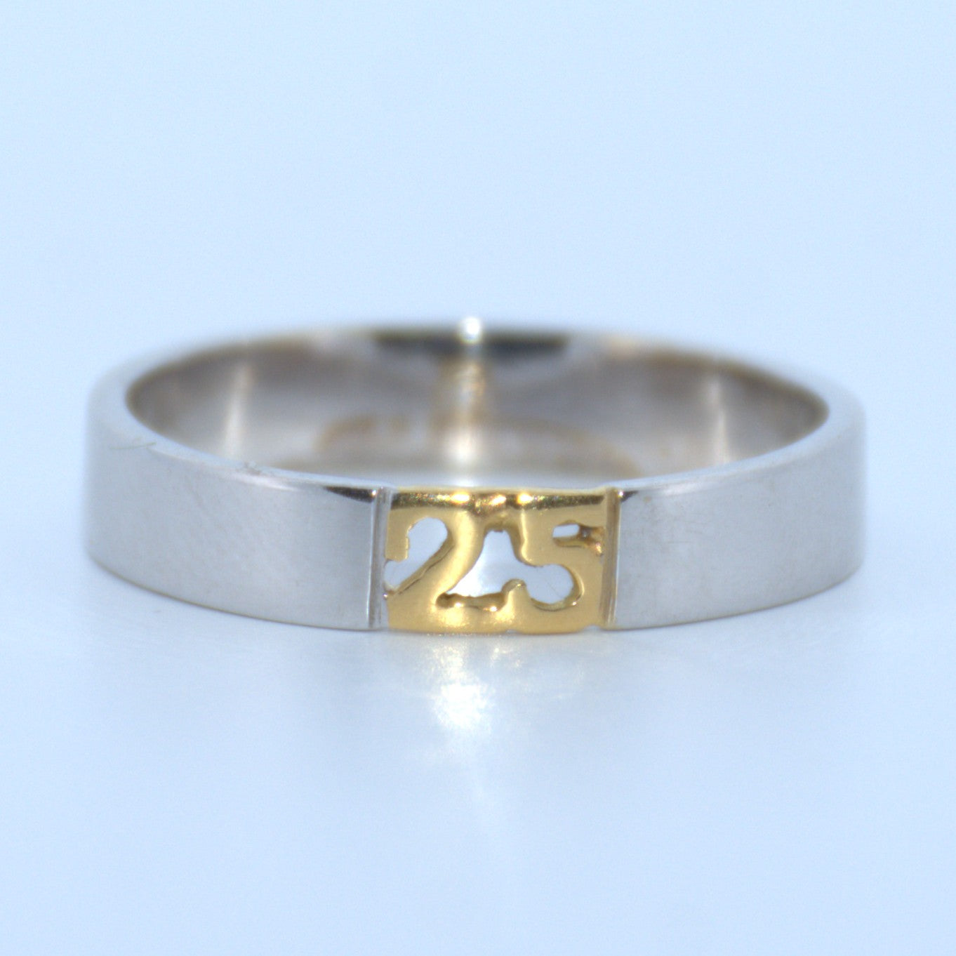 Silver ring with a gold '25' cutout on a light blue background