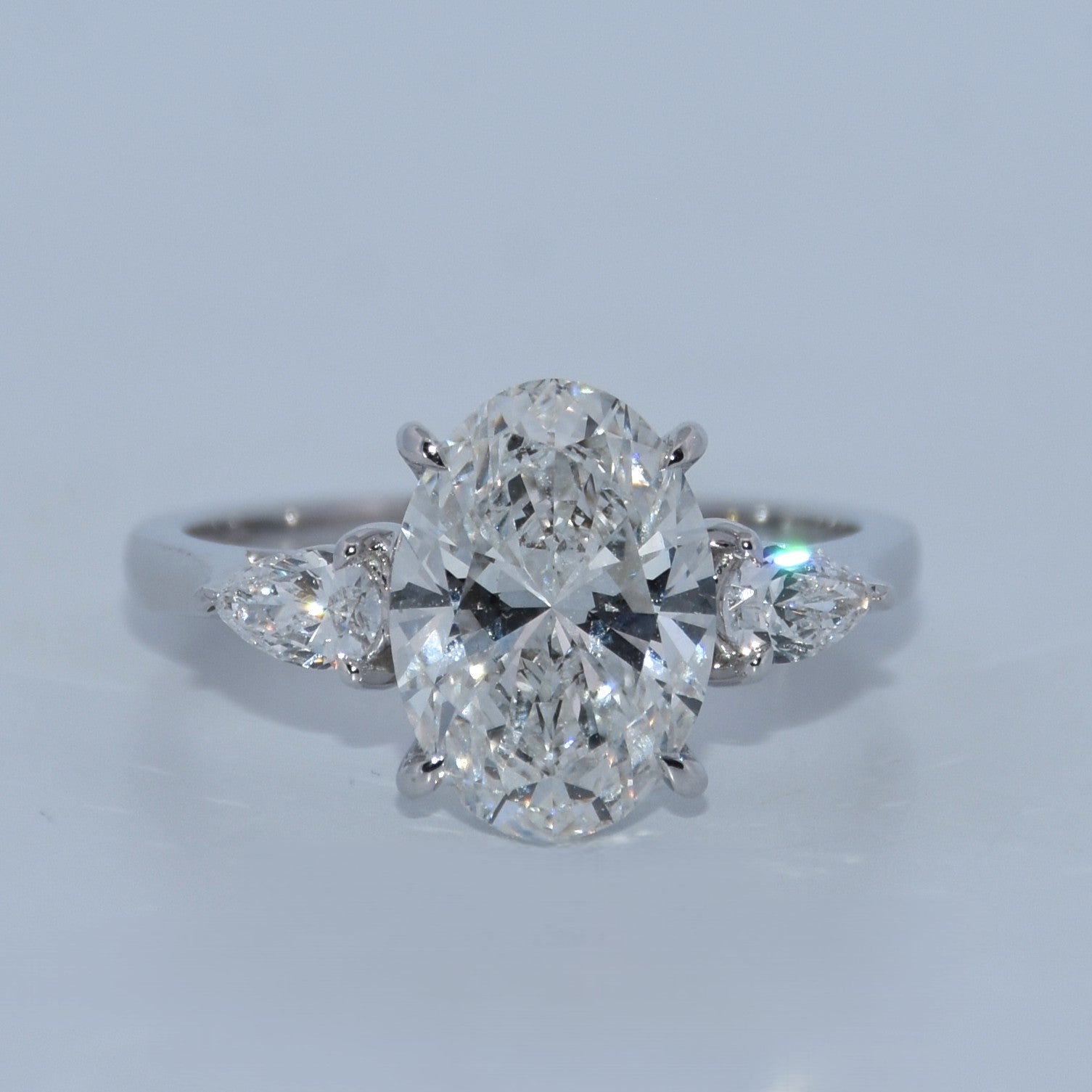Diamond ring with a pear-shaped center stone on a light gray background