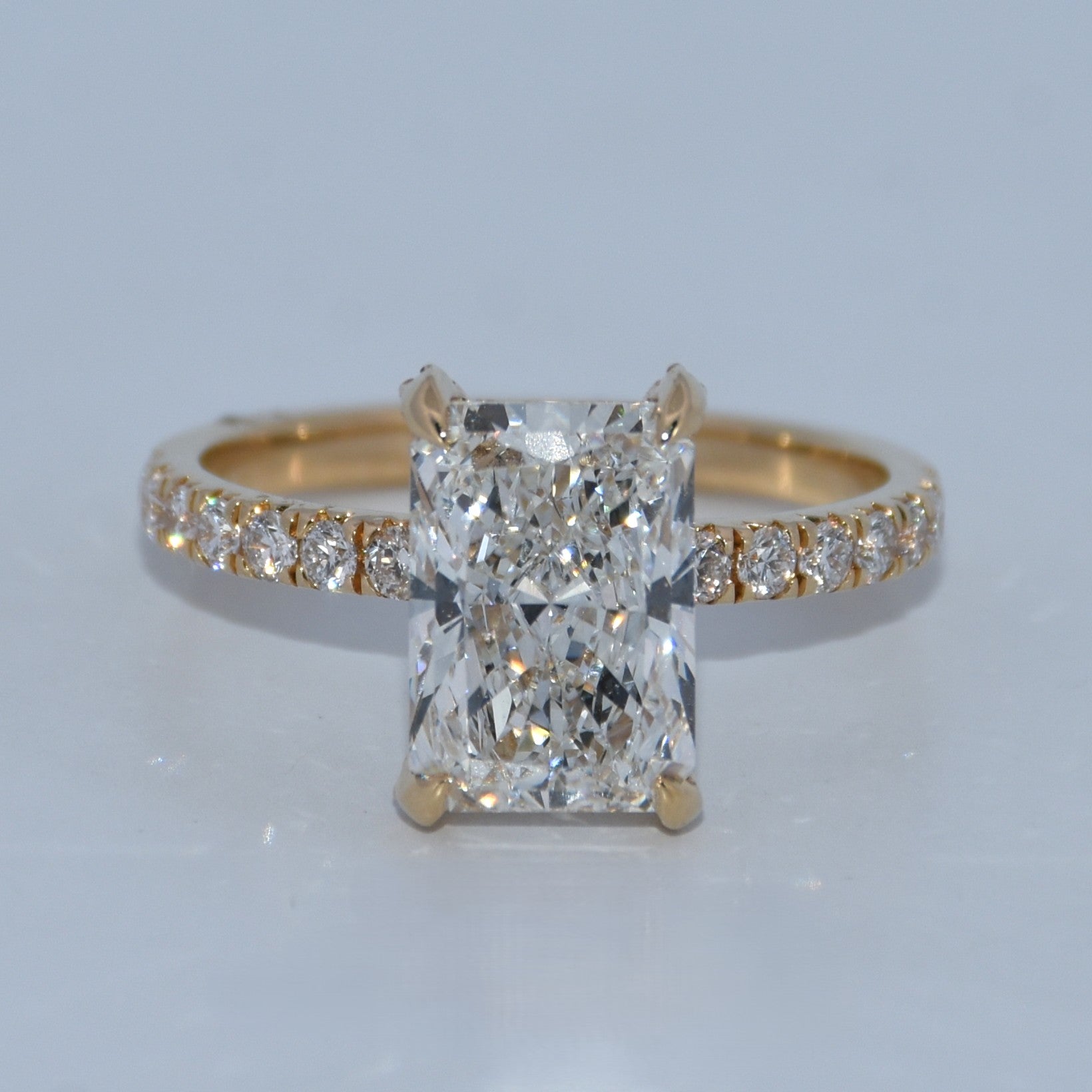 Gold ring with a large diamond and smaller diamonds on the band against a light gray background