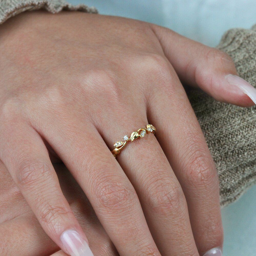 Gold ring with small diamonds on a person's finger against a neutral background