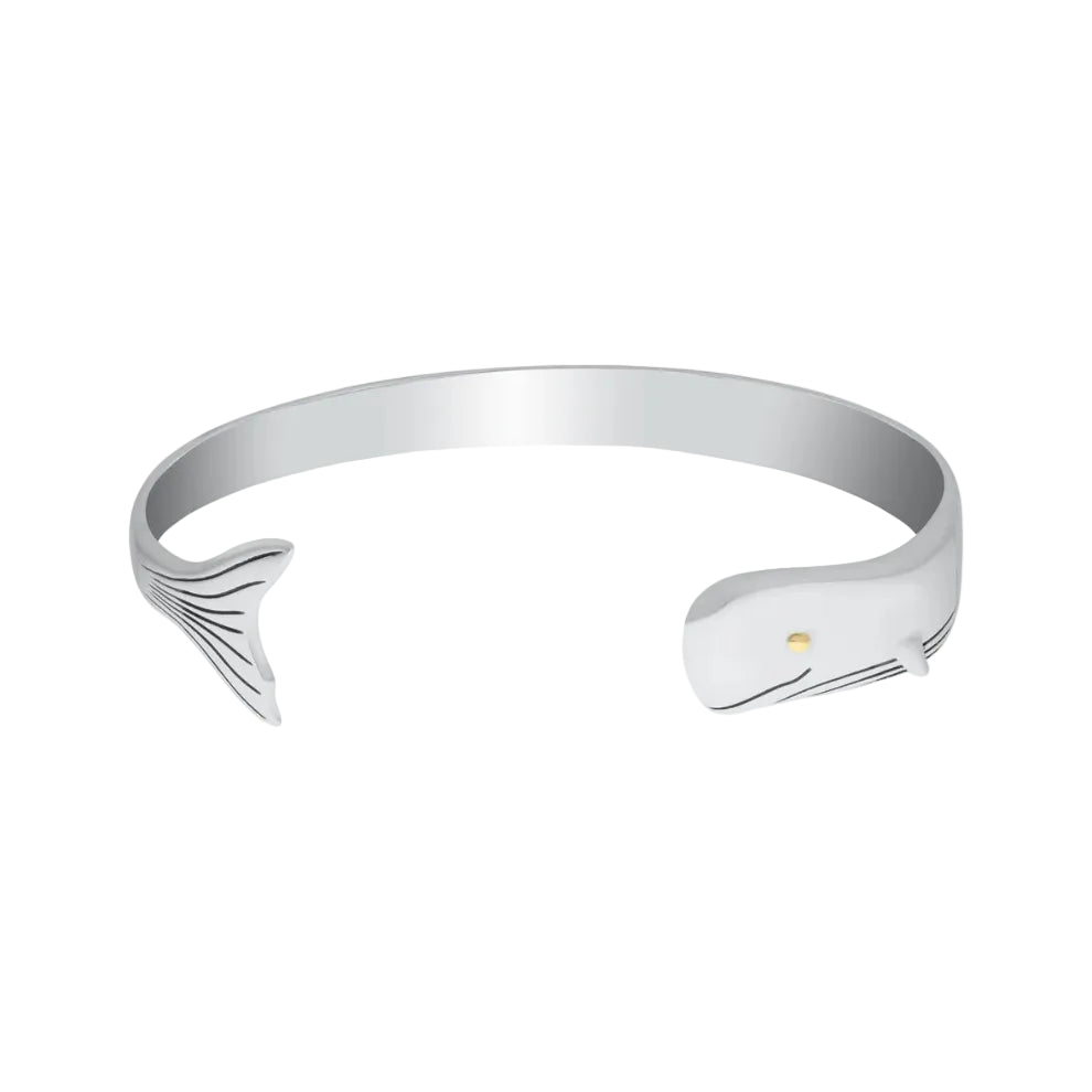 A silver-toned cuff bracelet shaped like a whale, featuring a whale tail on one end and a whale head on the other, with a tiny gold eye detail, shown on a plain white background.