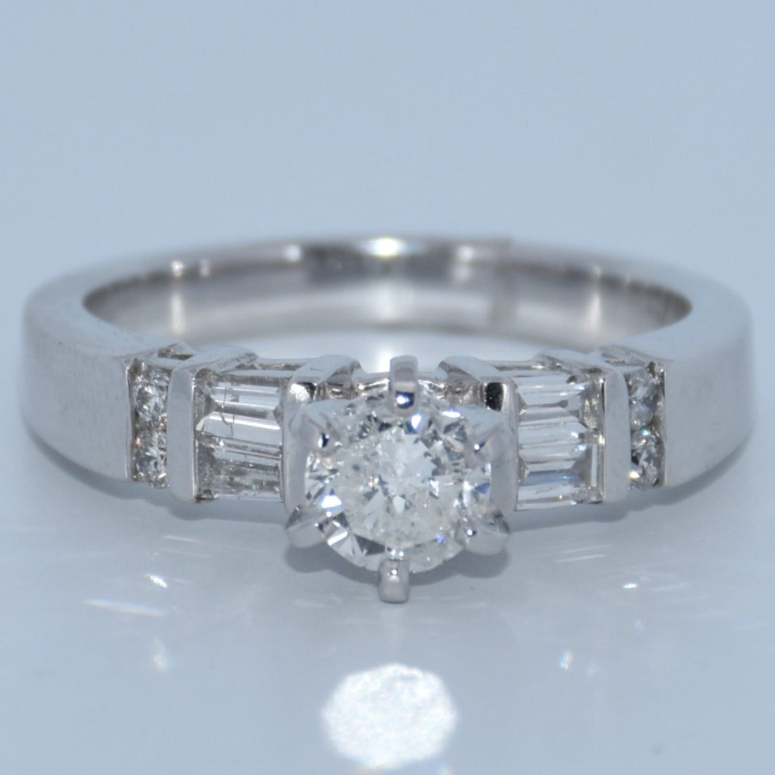 Diamond ring with a central diamond and baguette-cut side stones on a light gray background
