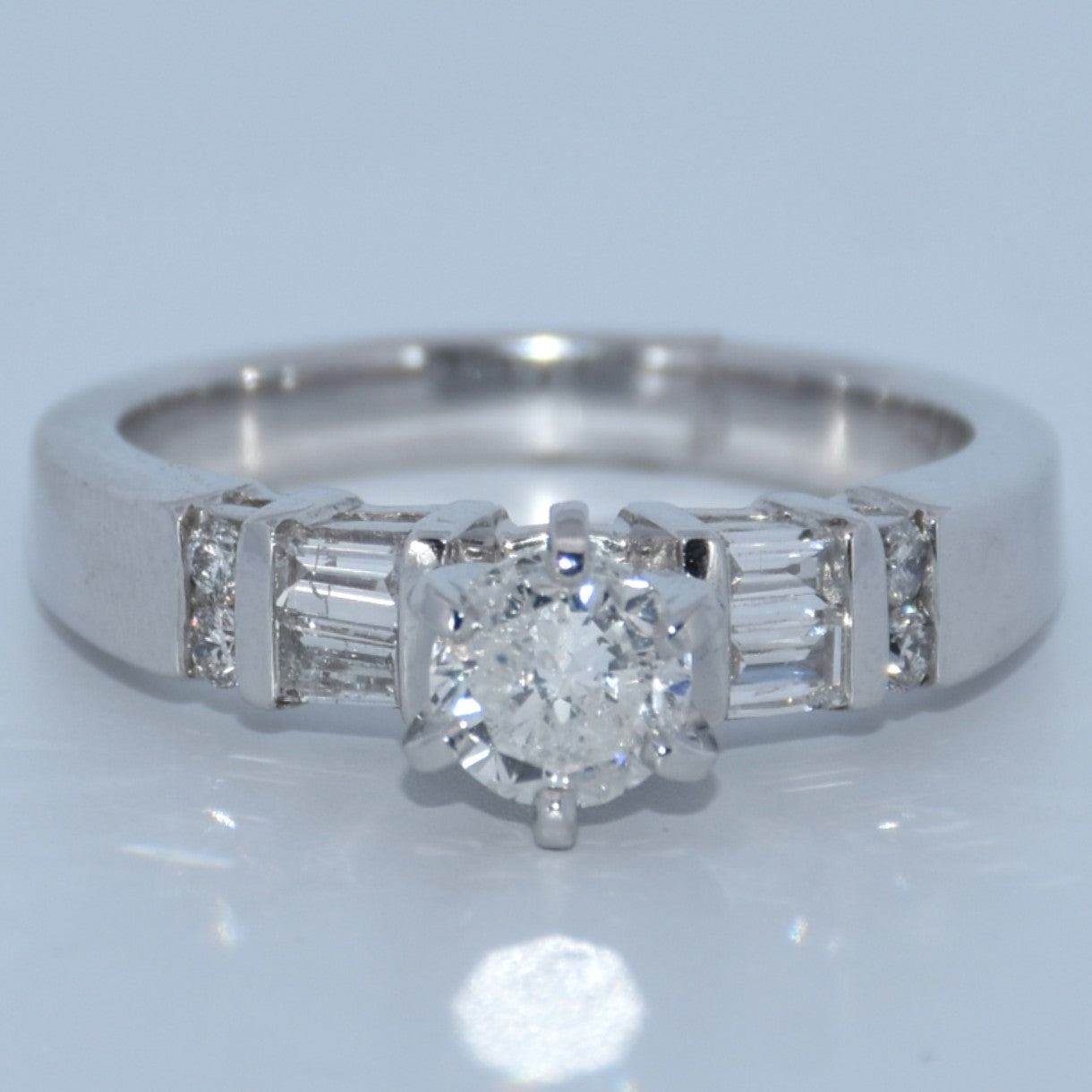 Diamond ring with a central diamond and baguette-cut side stones on a light gray background