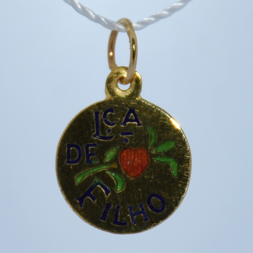 Gold pendant with 'LCA DE FILHO' text and heart design on a light blue background