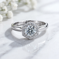 Silver ring with a diamond on a marble surface with white flowers in the background