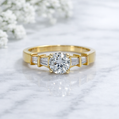 Gold ring with a large diamond and smaller baguette-cut diamonds on a light background