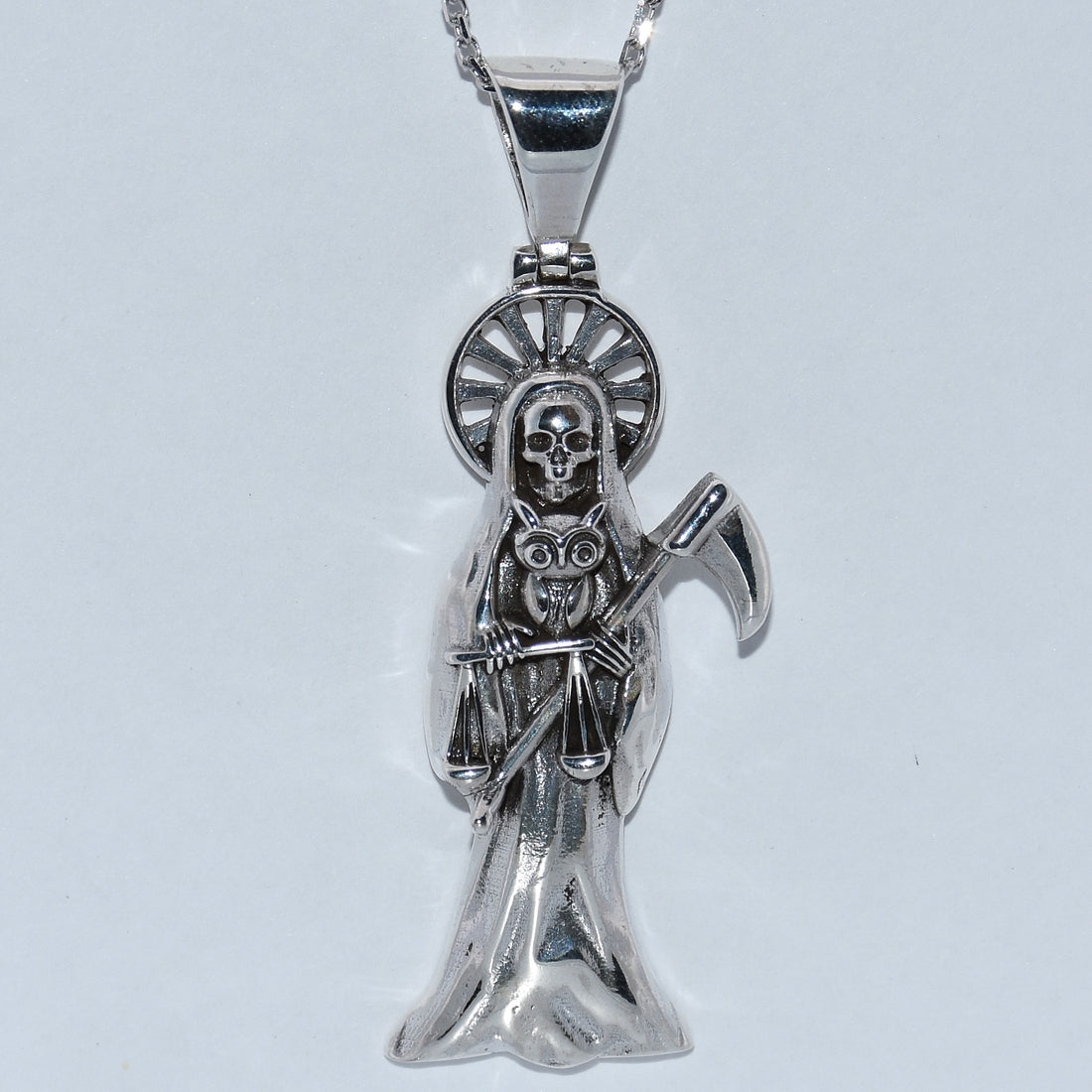 Silver pendant with a skeleton figure holding an owl on a white background