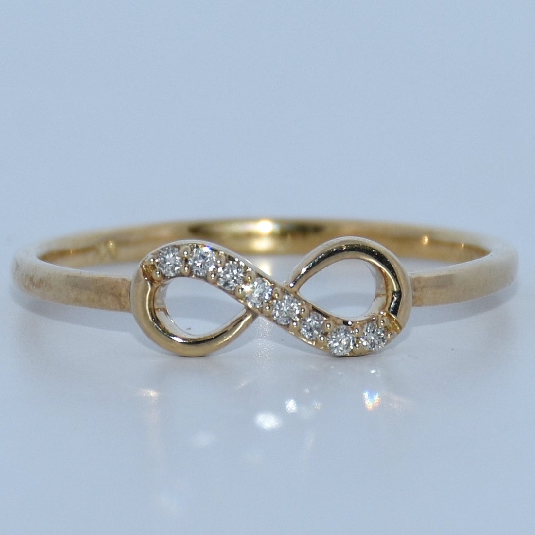 Gold infinity ring with diamonds on a light gray background