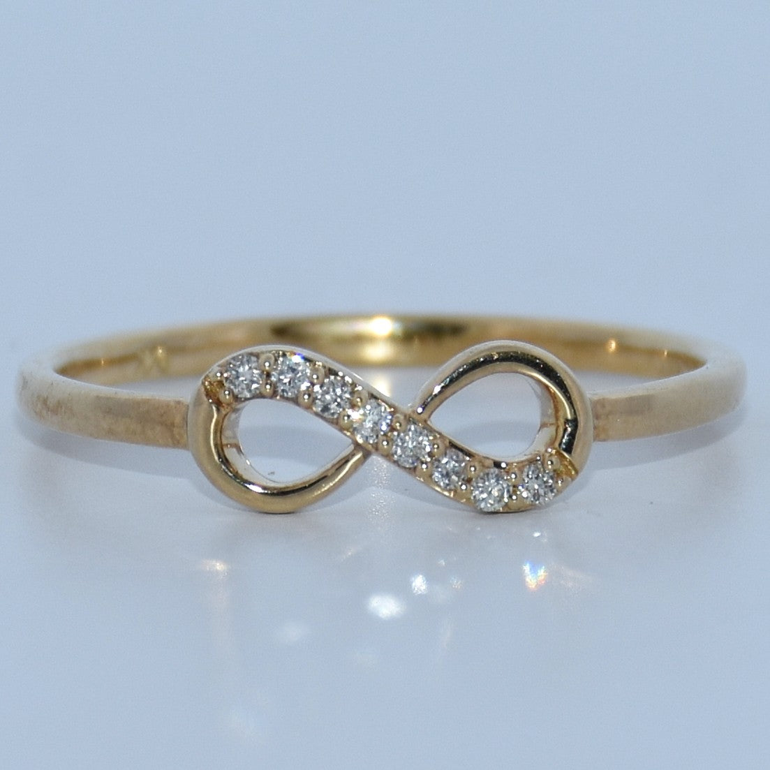 Gold infinity ring with diamonds on a light gray background