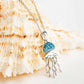 A silver jellyfish pendant necklace with a bright blue rhinestone-studded top, displayed on a large beige seashell against a clean white background. Ocean | Deep Blue Sterling Silver Aqua Crystal Jellyfish Necklace