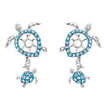 A pair of silver-toned turtle drop earrings embellished with bright blue rhinestones, shown on a plain white background.