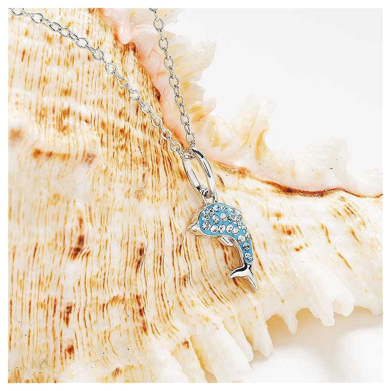 A silver chain necklace with a dolphin pendant adorned with light blue rhinestones, displayed on a large beige seashell against a white background.