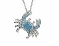 A silver-toned crab pendant necklace adorned with light blue rhinestones and clear crystals, hanging from a silver chain against a plain white background.