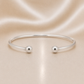 Silver bracelet with two spherical charms on a beige fabric background Sterling Silver | Ball Bangle Bracelet