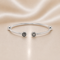 Silver bracelet with spiral designs on a beige satin background Sterling Silver | CHAM Bypass Charm Bangle Bracelet