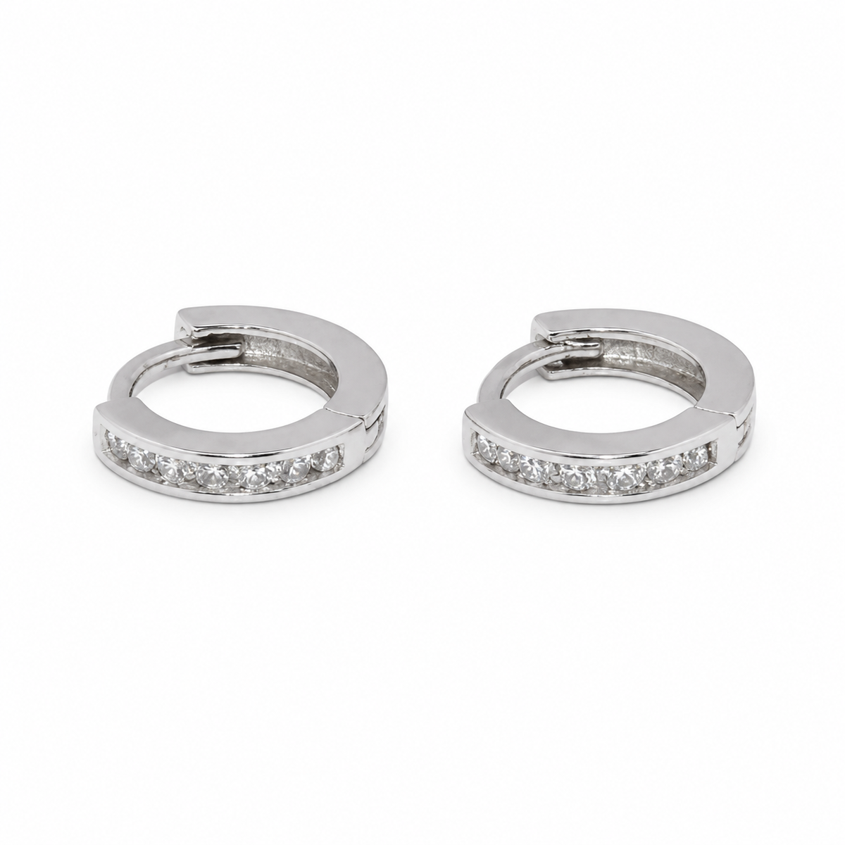 A pair of silver huggie hoop earrings with a row of clear pavé-set stones along the front, displayed on a clean white background.