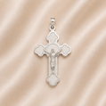 Silver cross pendant with Jesus Christ figure on a pink satin  Sterling Silver | High Polished with Matte Finish Crucifix Pendant background