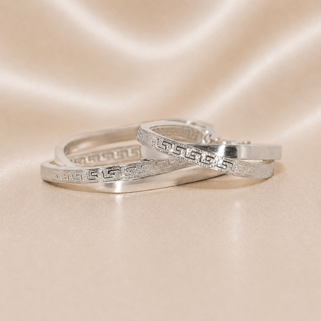Two silver rings with intricate designs on a beige satin background Sterling Silver | Oval Greek Key Design Hoops