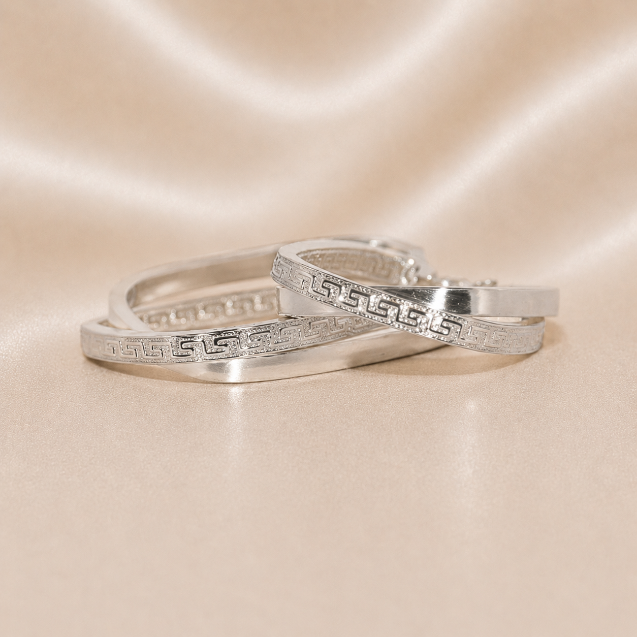 Two silver rings with intricate designs on a beige satin background Sterling Silver | Oval Greek Key Design Hoops