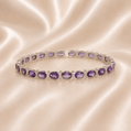 Silver bracelet with purple gemstones on a satin surface Sterling Silver | Round & Oval Amethyst Hinged Link Bangle Bracelet