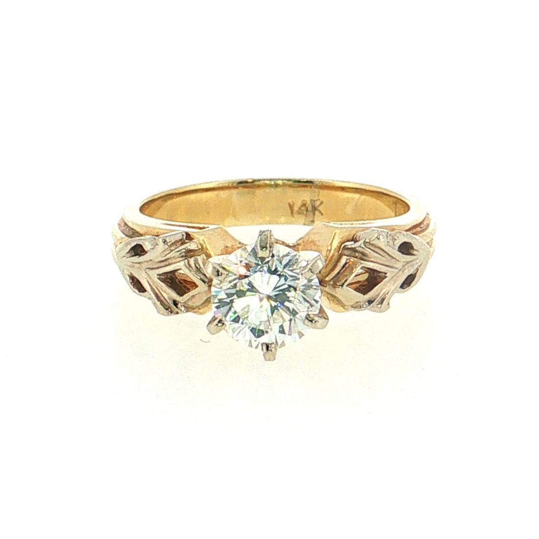 A yellow gold ring with a round-cut clear gemstone and decorative geometric side settings, shown on a plain white background.