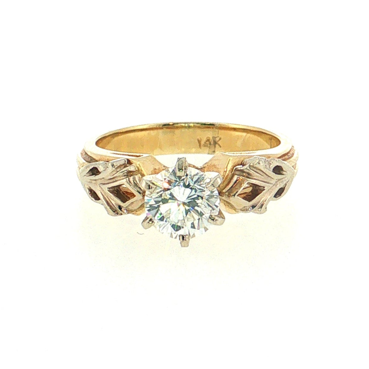 A yellow gold ring with a round-cut clear gemstone and decorative geometric side settings, shown on a plain white background.