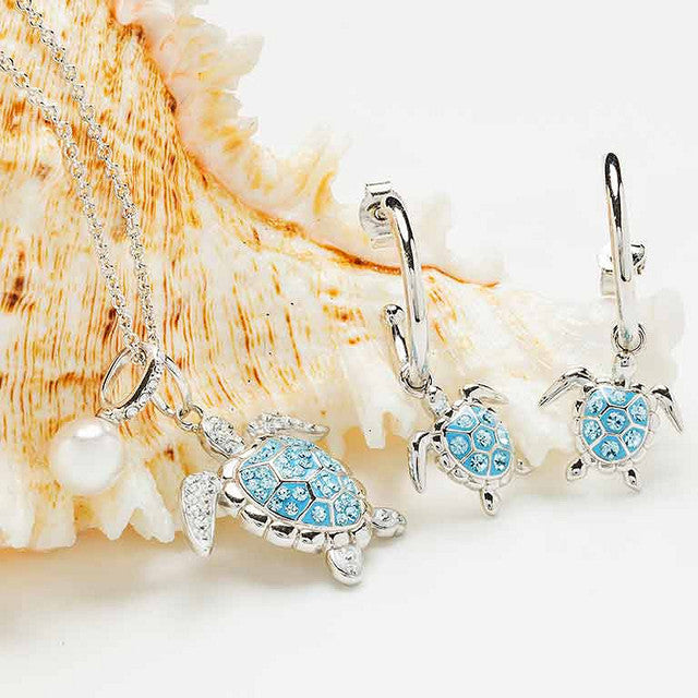 Silver-toned jewelry set featuring a necklace and matching earrings with sea turtle charms. The turtle pendants have light blue enamel-style detailing and are accented with small clear rhinestones.